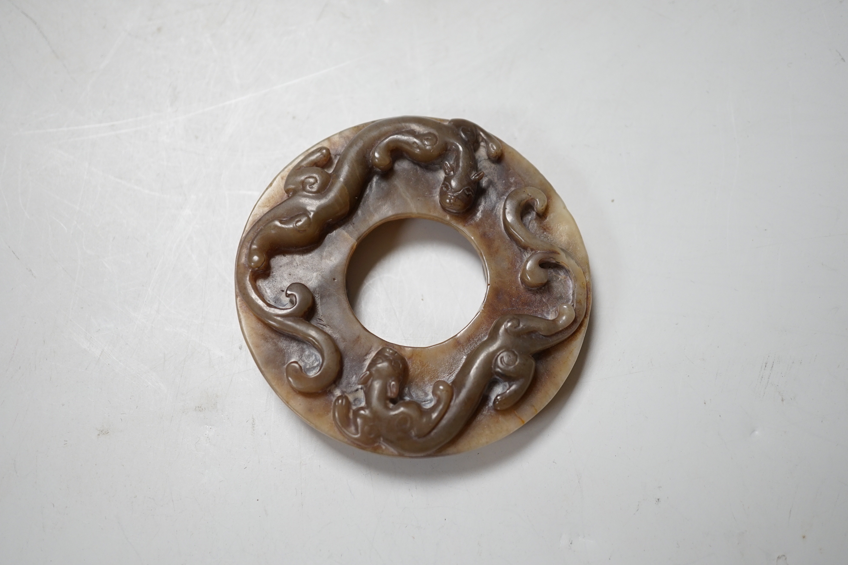 A Chinese brown and celadon jade ‘chilong’ bi disc, probably Ming dynasty, 8cm